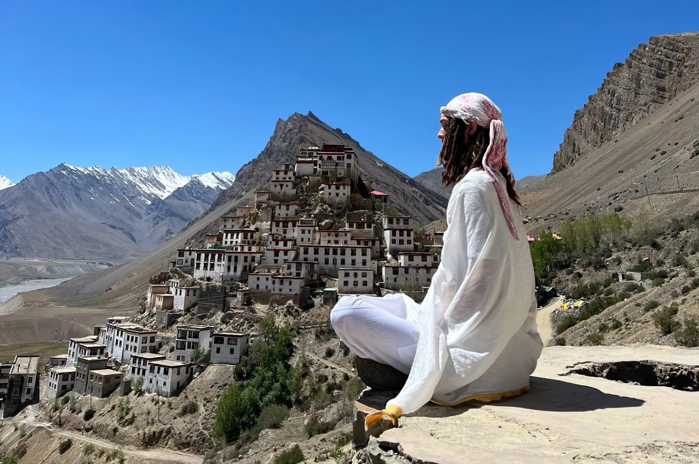 Hunter in white robes meditating on a cliff above Key Monastery, Spiti Valley, in the Himalayas.