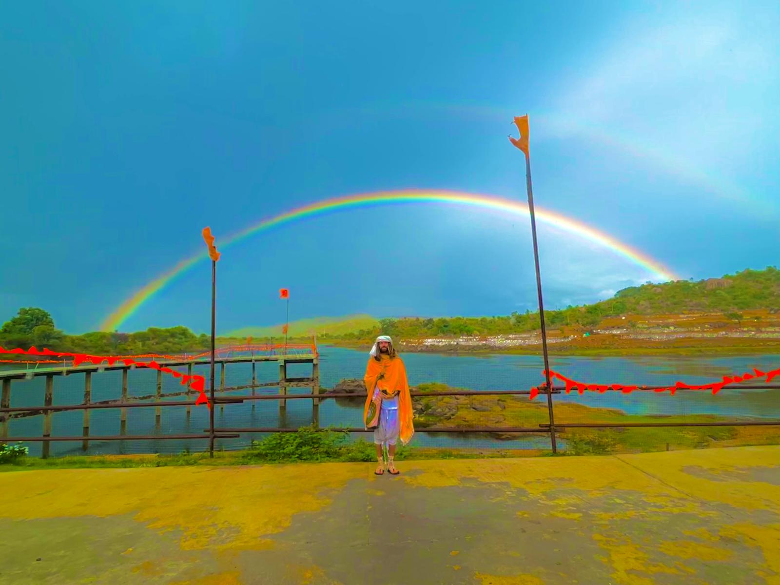 Hunter in orange robes beneath a full double rainbow at the river ghat in Penukonda, India.