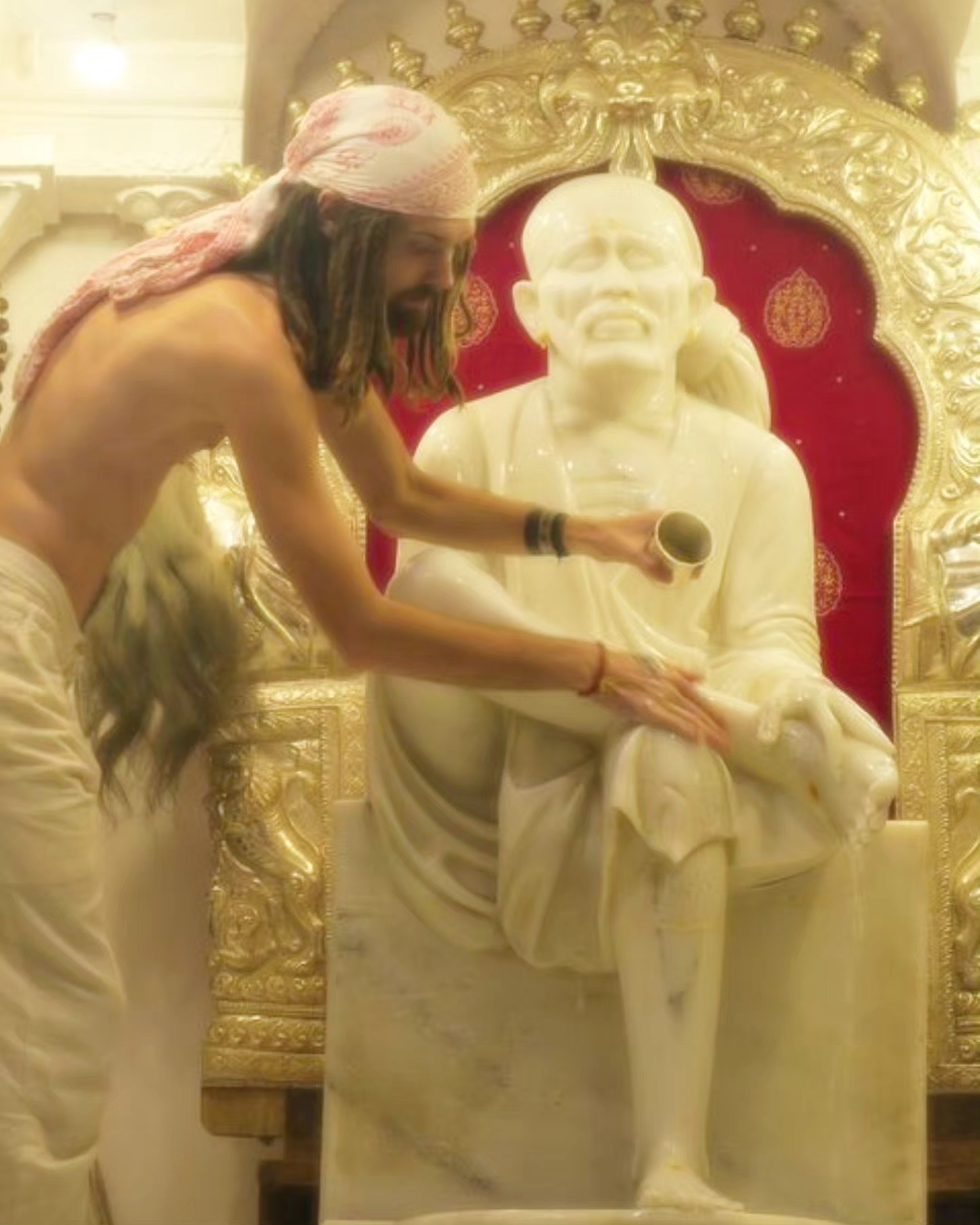 Hunter performing abhishekam, bathing the white marble murti of Shirdi Sai Baba in a golden temple shrine.