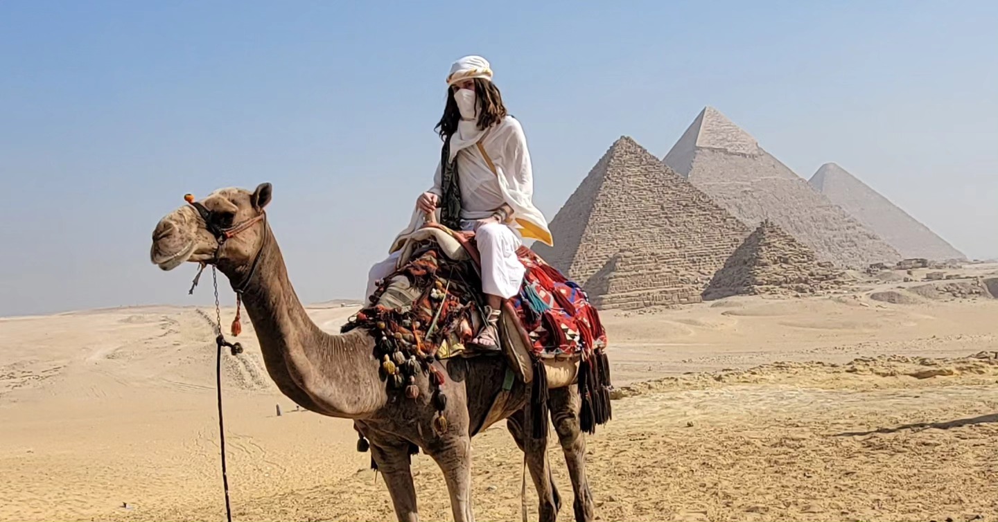 Isa, veiled in white, riding a camel before the Great Pyramids of Giza.